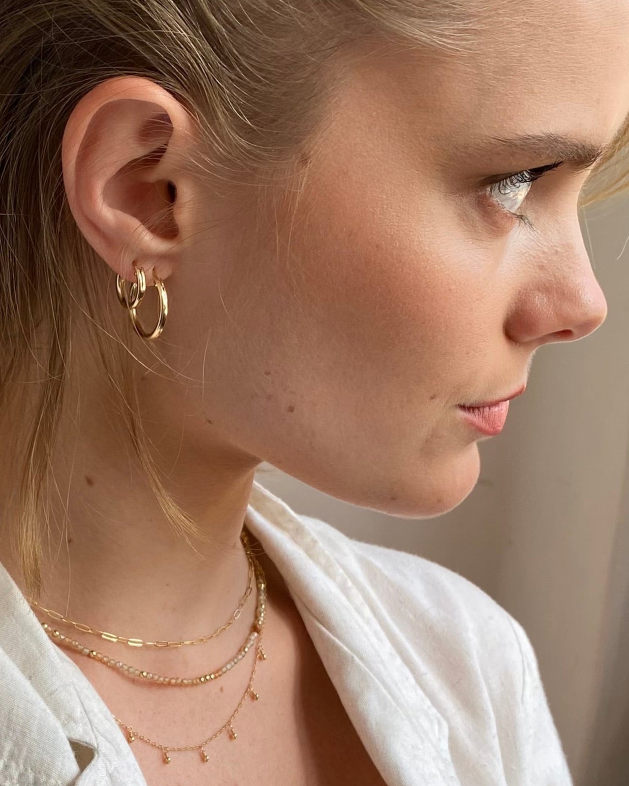 Close-up of a woman wearing gold hoop earrings and necklaces