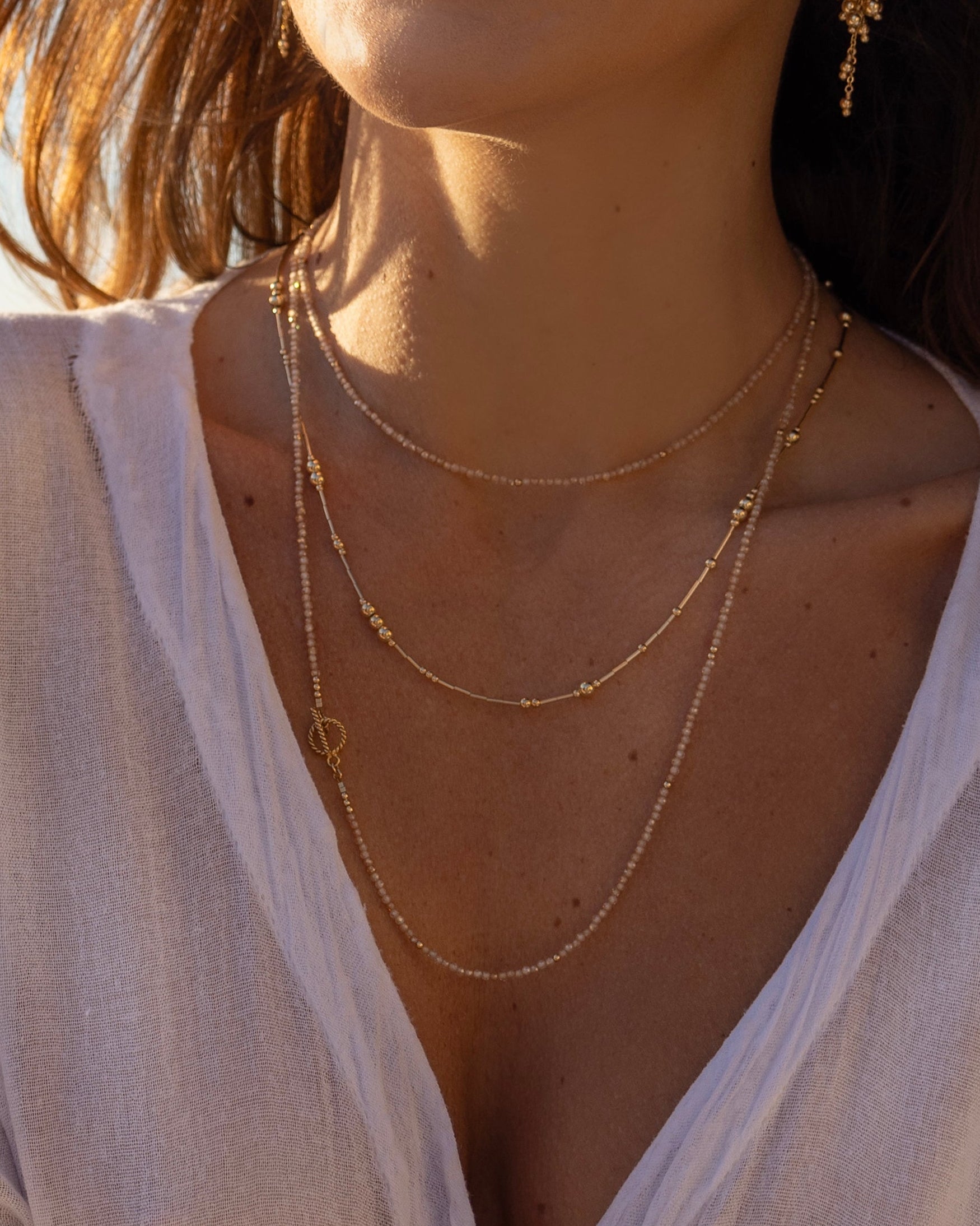 Woman wearing a delicate gold Dione Necklace from Corali and earrings