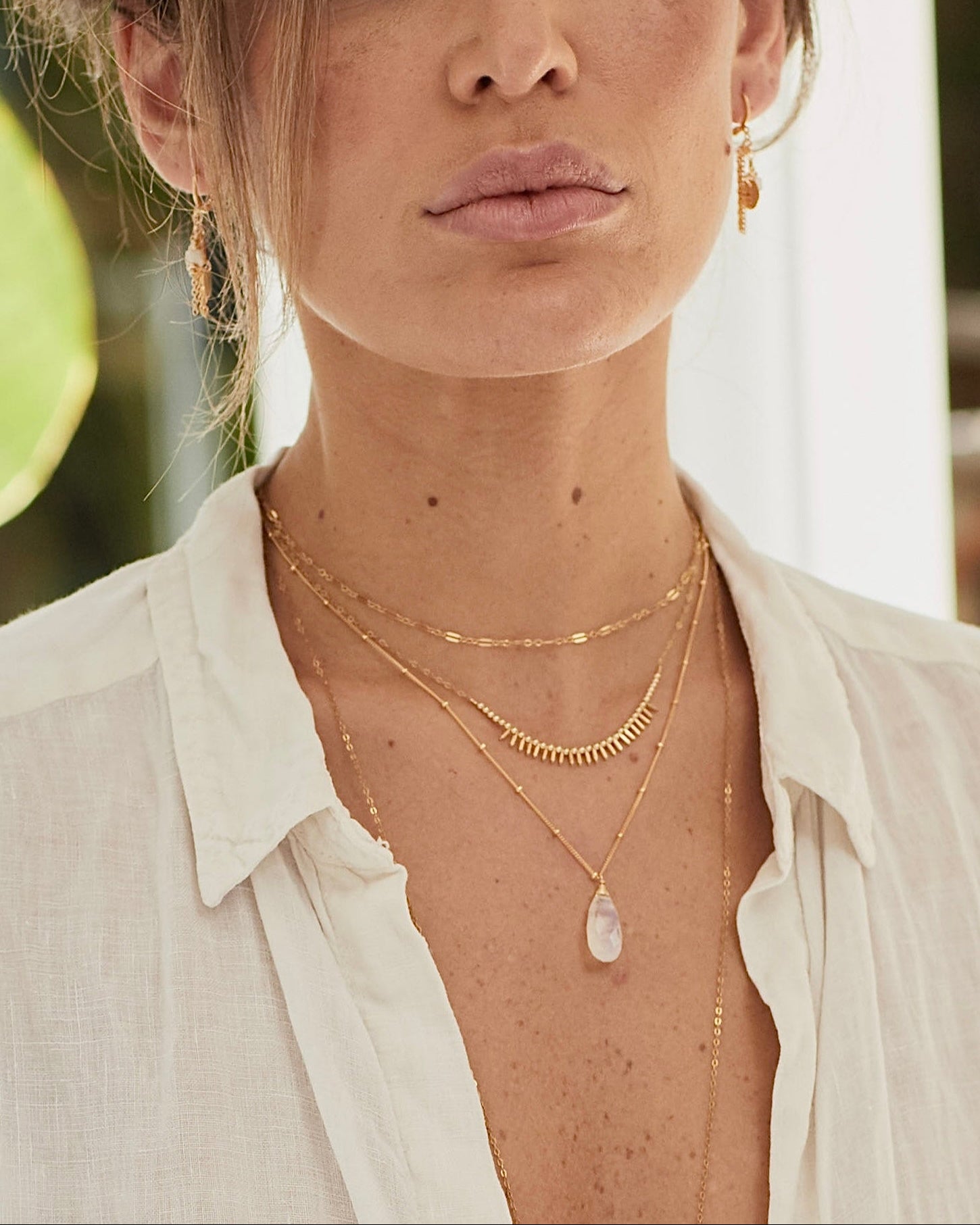 Close-up of a person wearing gold necklaces and earrings with a blurred background