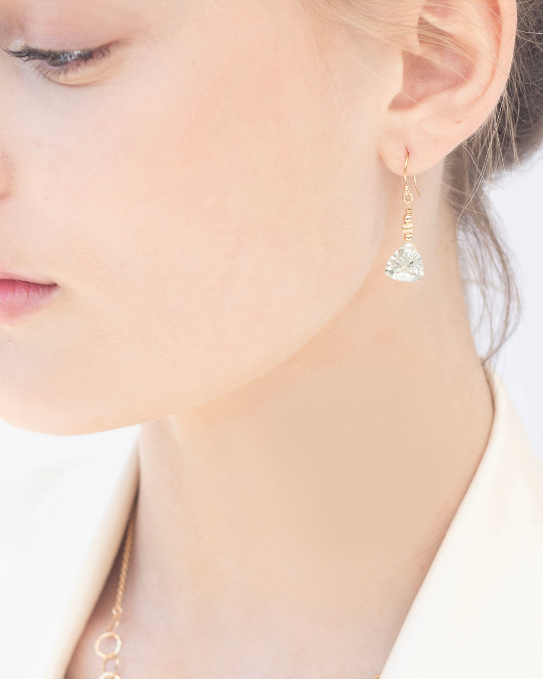 Close-up of a person wearing gold earrings with green amethyst faceted gemstones.