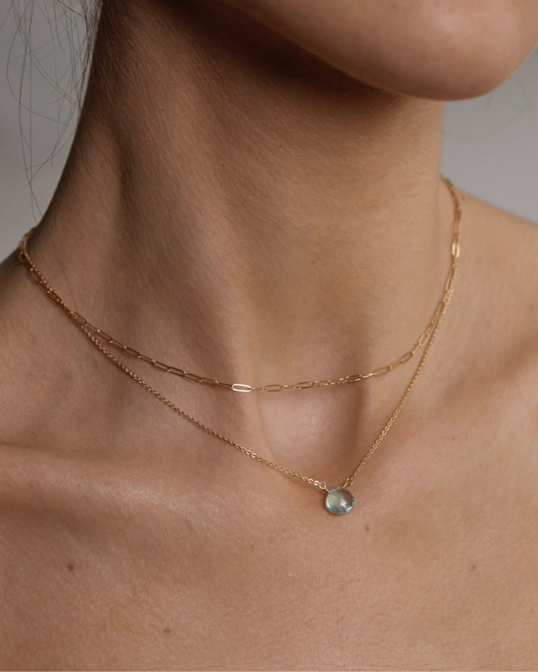 Close up of woman's neck with gold chain necklace with blue topaz teardrop pendant and link gold chain