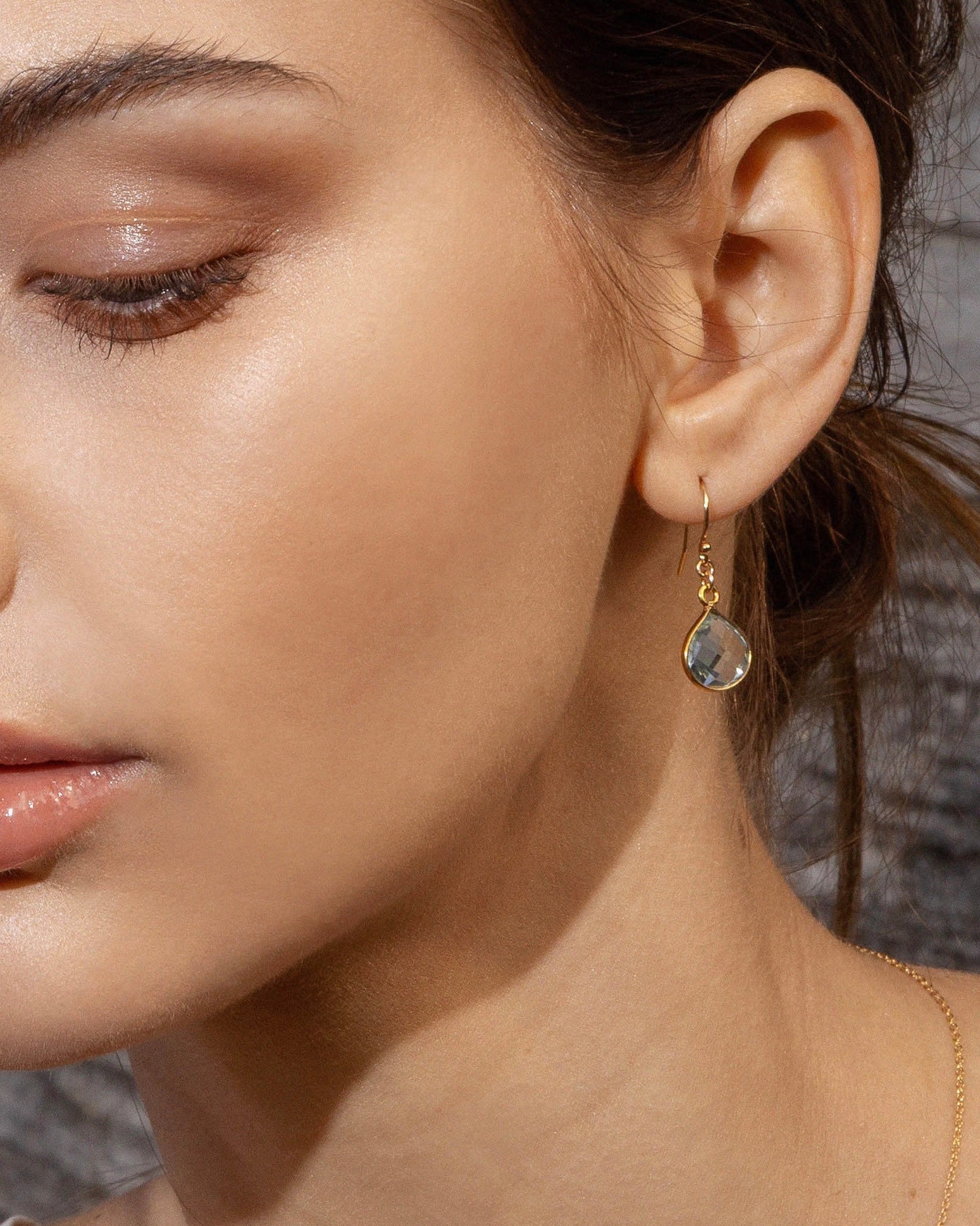 Close-up of a woman wearing gold earrings with blue topaz gemstone.