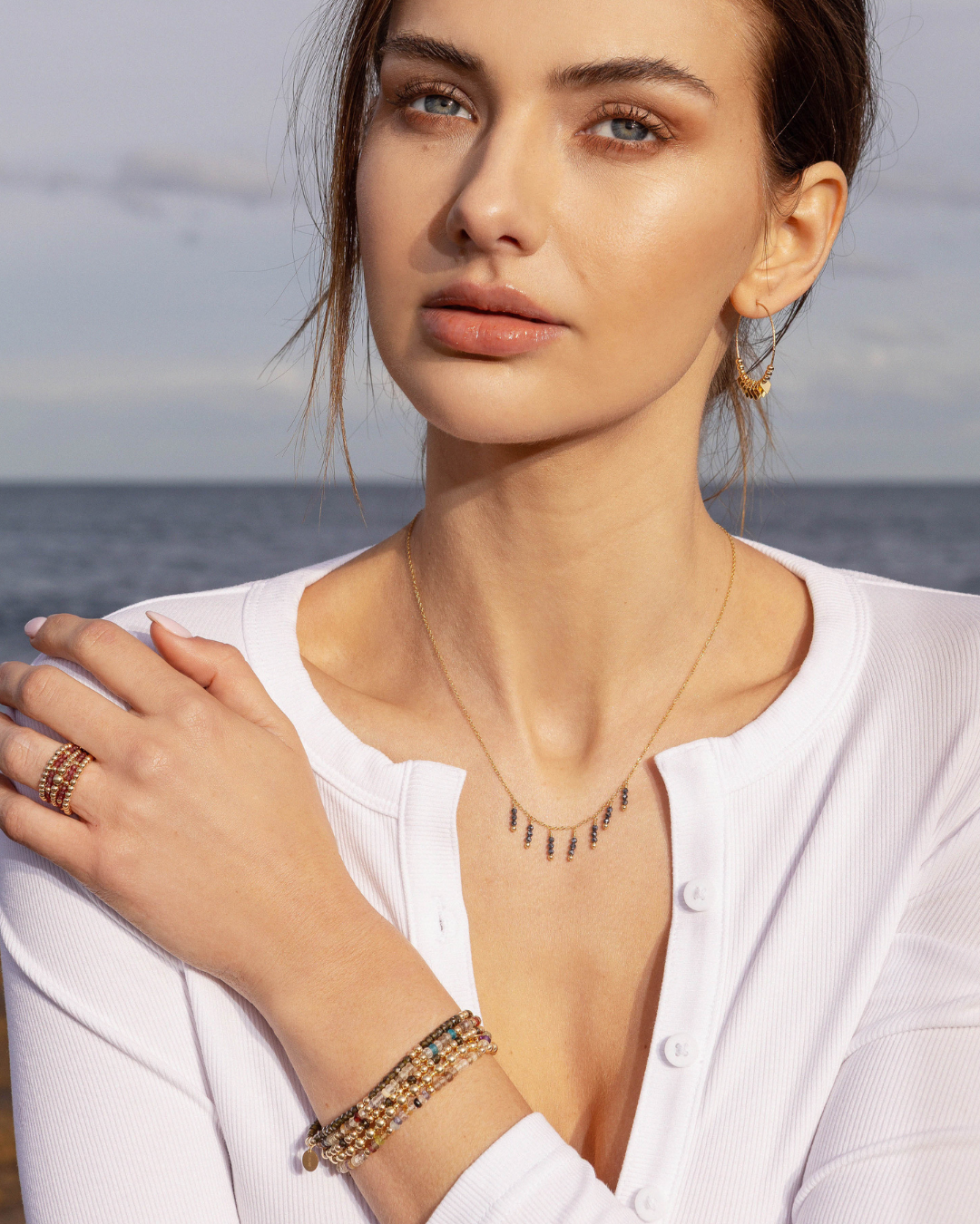 Woman wearing gold jewellery including a necklace with black spinel gemstones with an ocean background