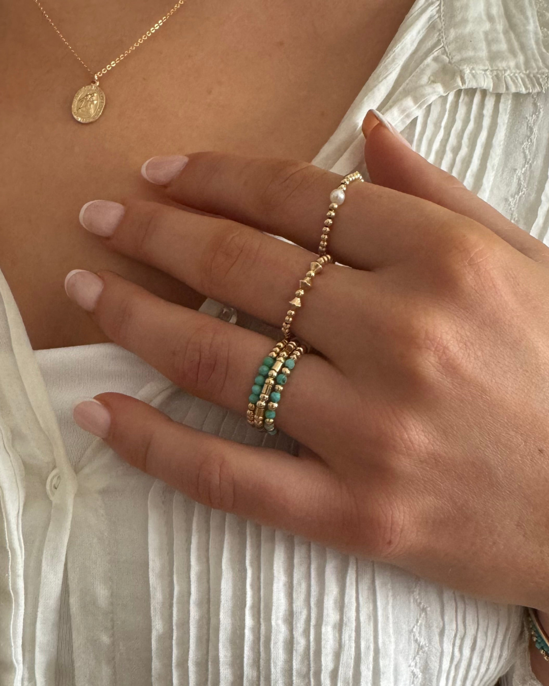Close-up of a hand wearing gold rings with gold beads and turquoise gemstones and a pear gold beaded ring.