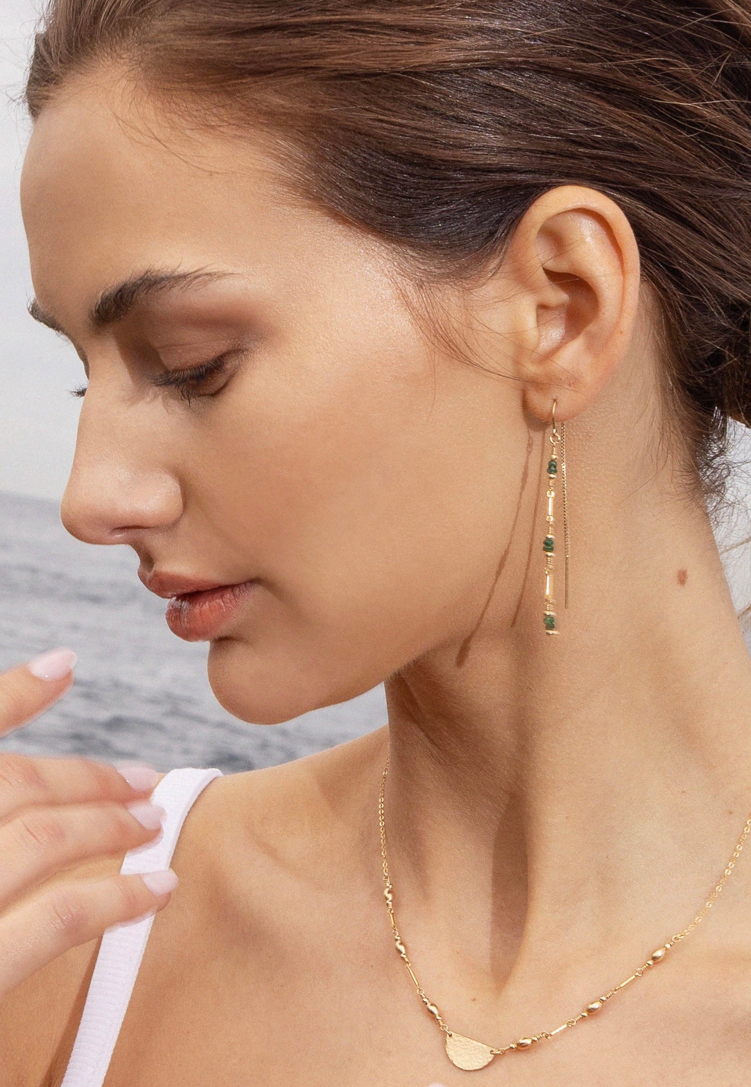 Woman wearing gold thread earrings with emerald gemstones and gold necklace with a blurred background