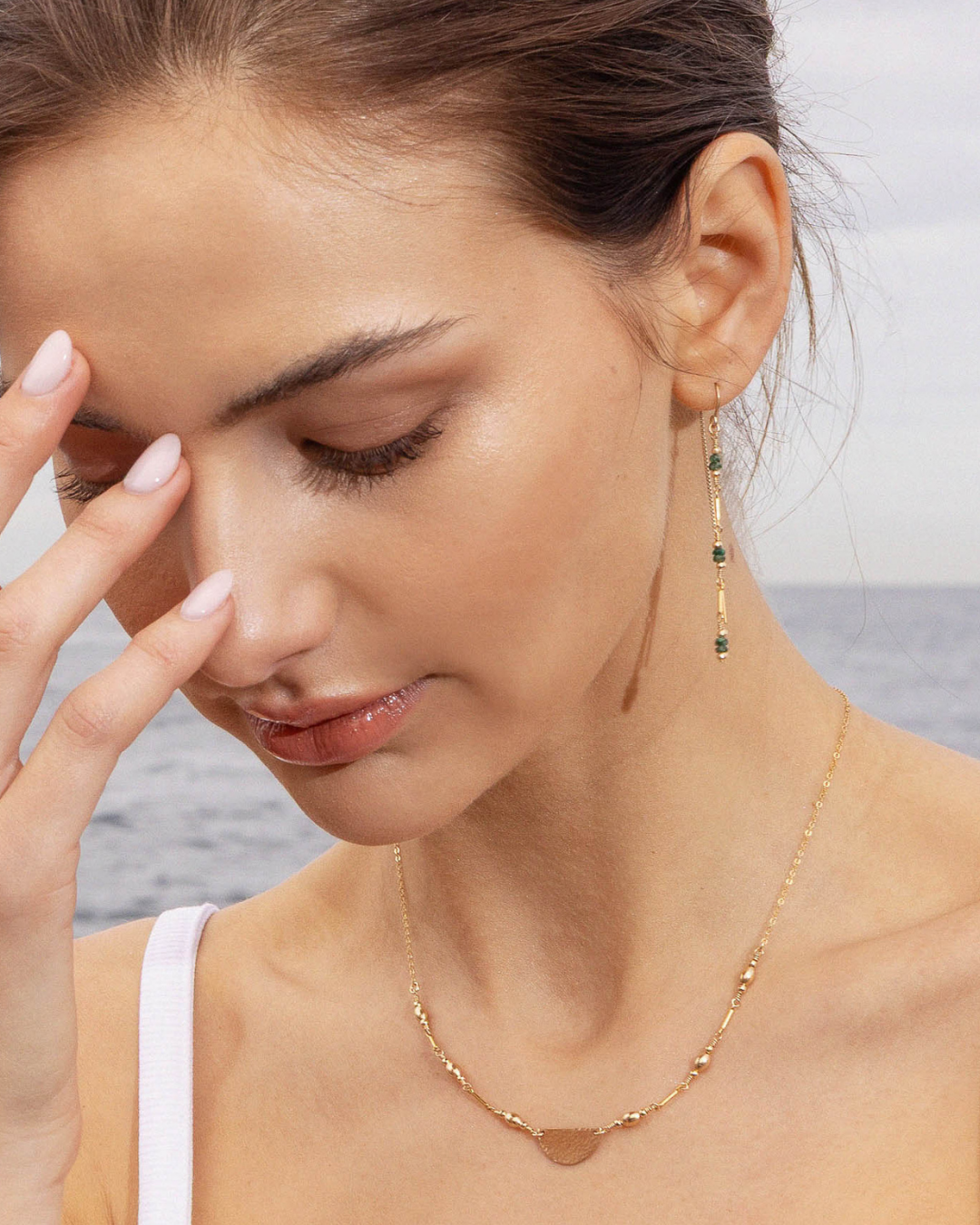 Woman wearing a gold necklace and earrings with green emerald gemstones and a blurred background