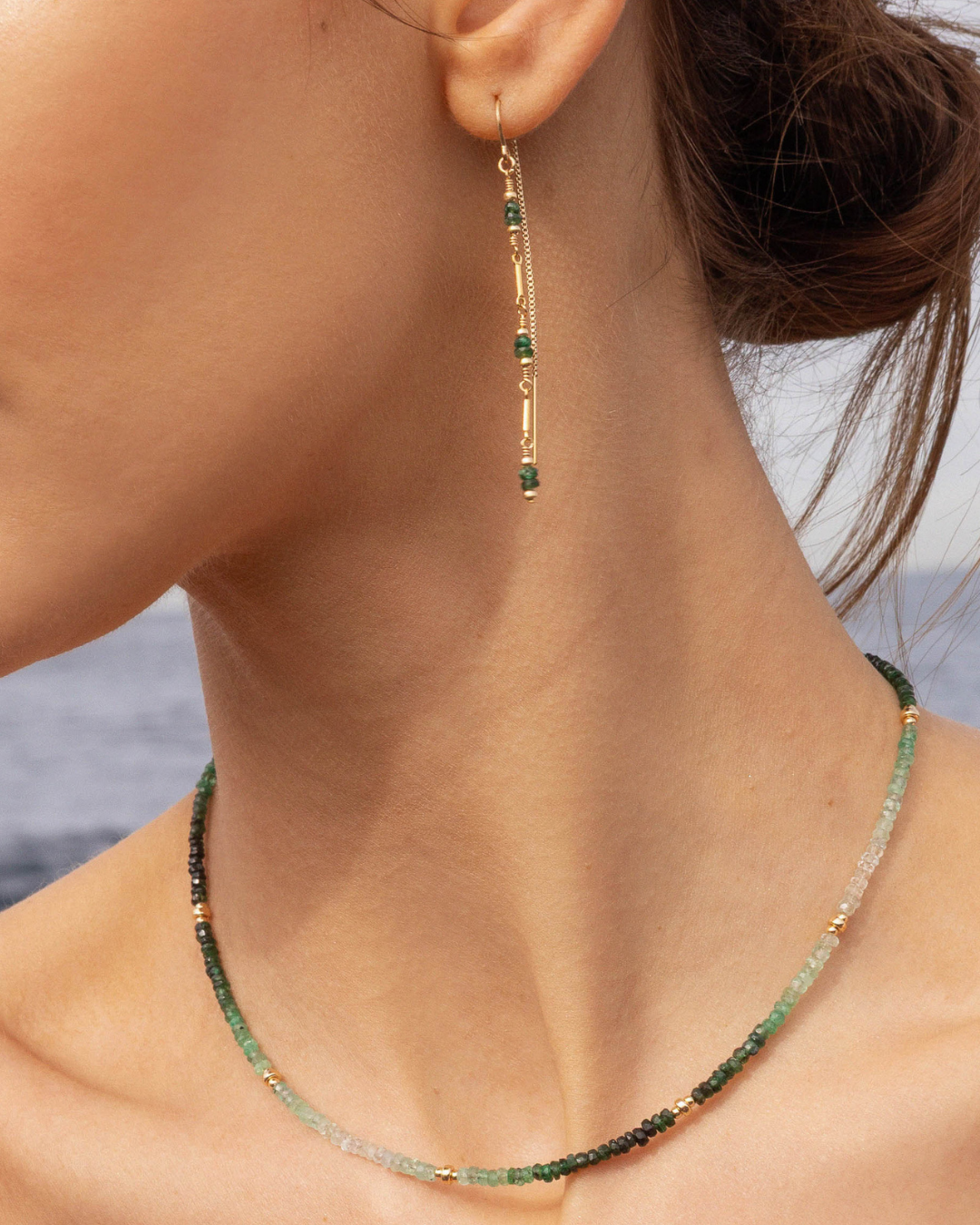 Close-up of a person wearing green emerald gemstone thread earrings and a green emerald necklace with blurred background