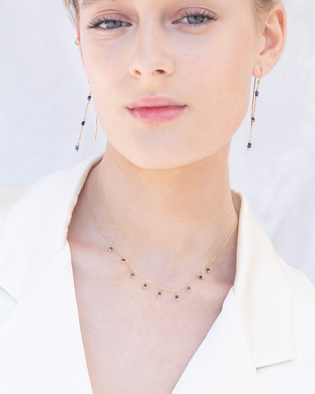 Close-up of a person wearing a sapphire gemstone delicate necklace and earrings on a light background