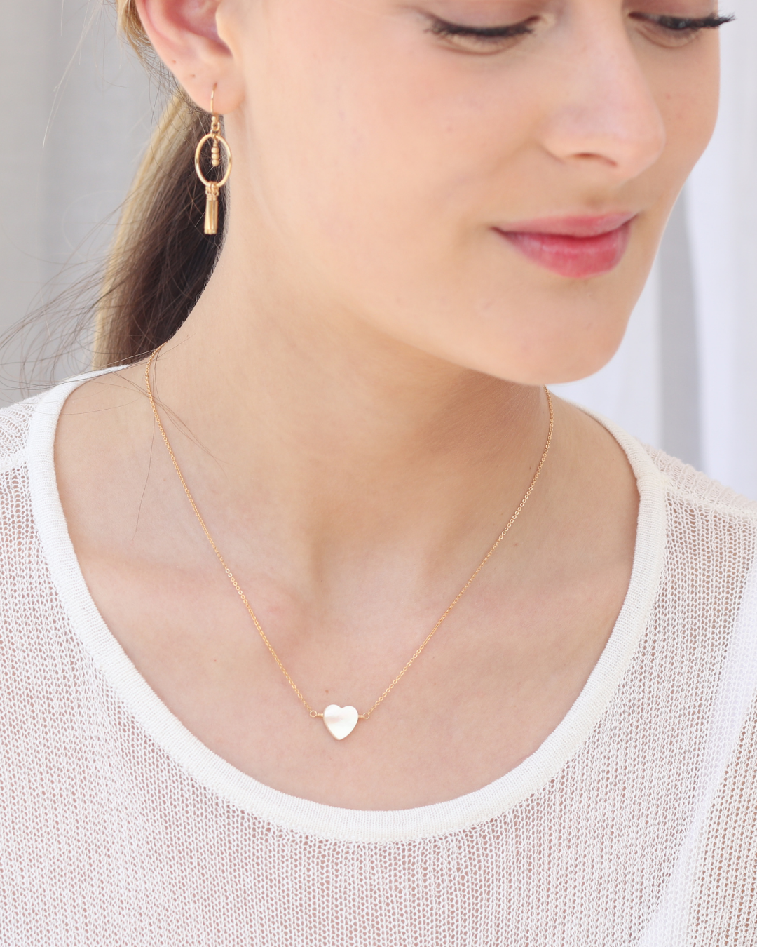 Close up of a model with a gold necklace with a heart shaped mother of pearl pendant and gold earrings.
