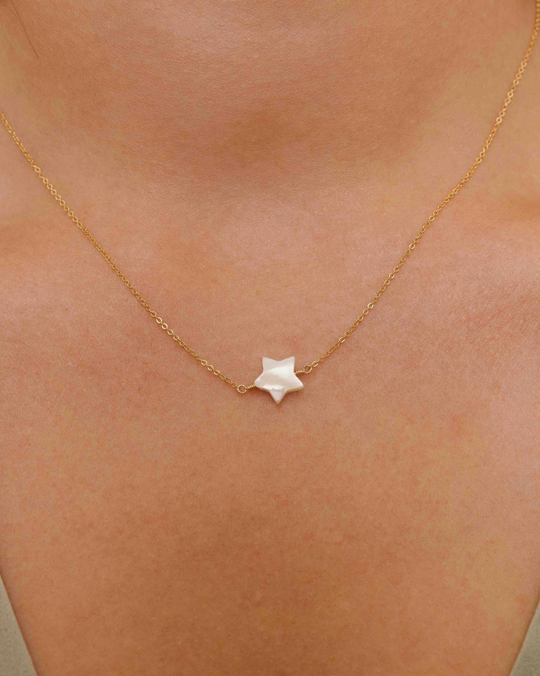 Close up of neck with gold necklace with a star-shaped mother of pearl pendant.