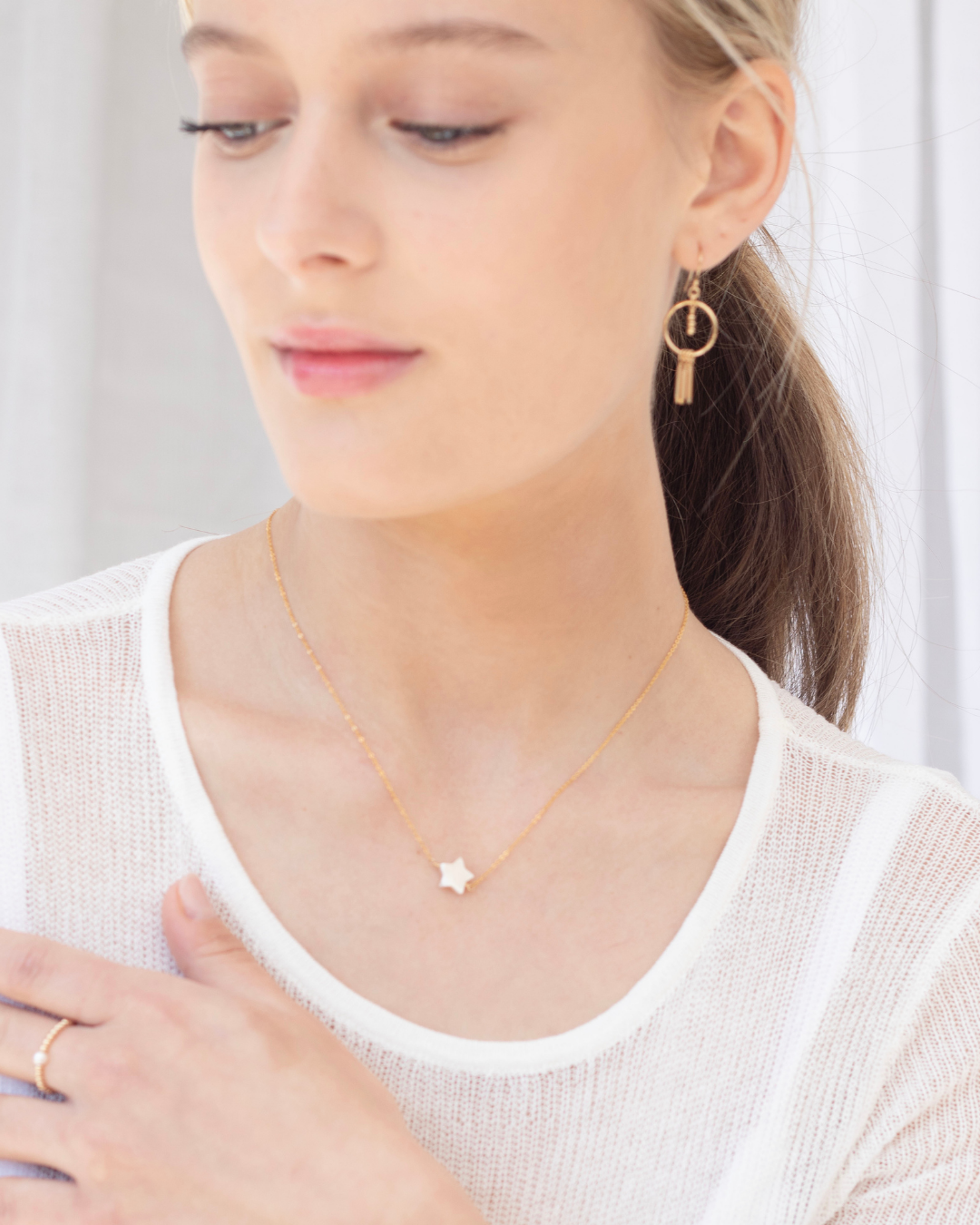 Woman wearing a gold necklace with a mother of pearl star pendant and gold drop earrings.