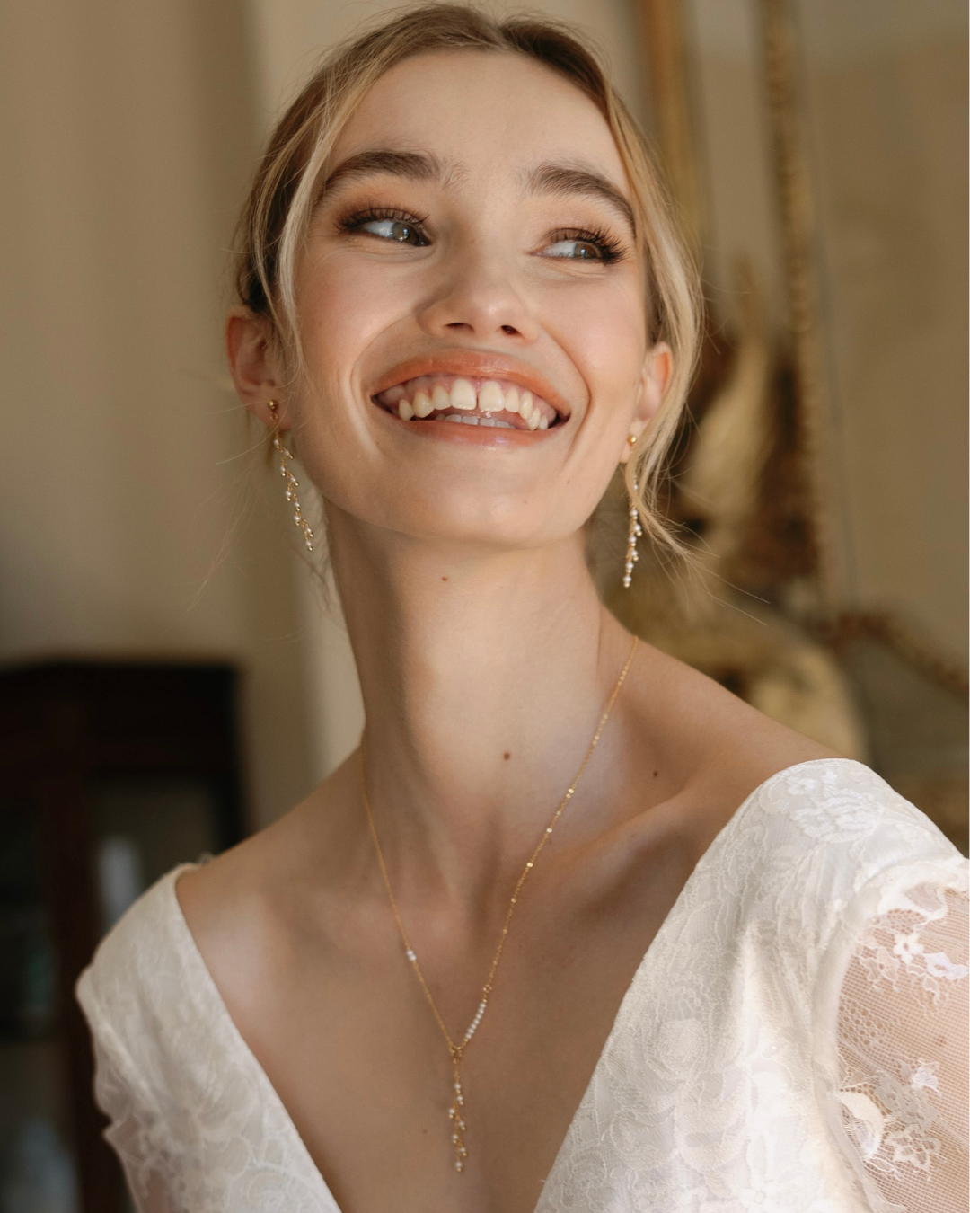 Bride wearing a gold and pearl necklace and earrings, smiling with a blurred background