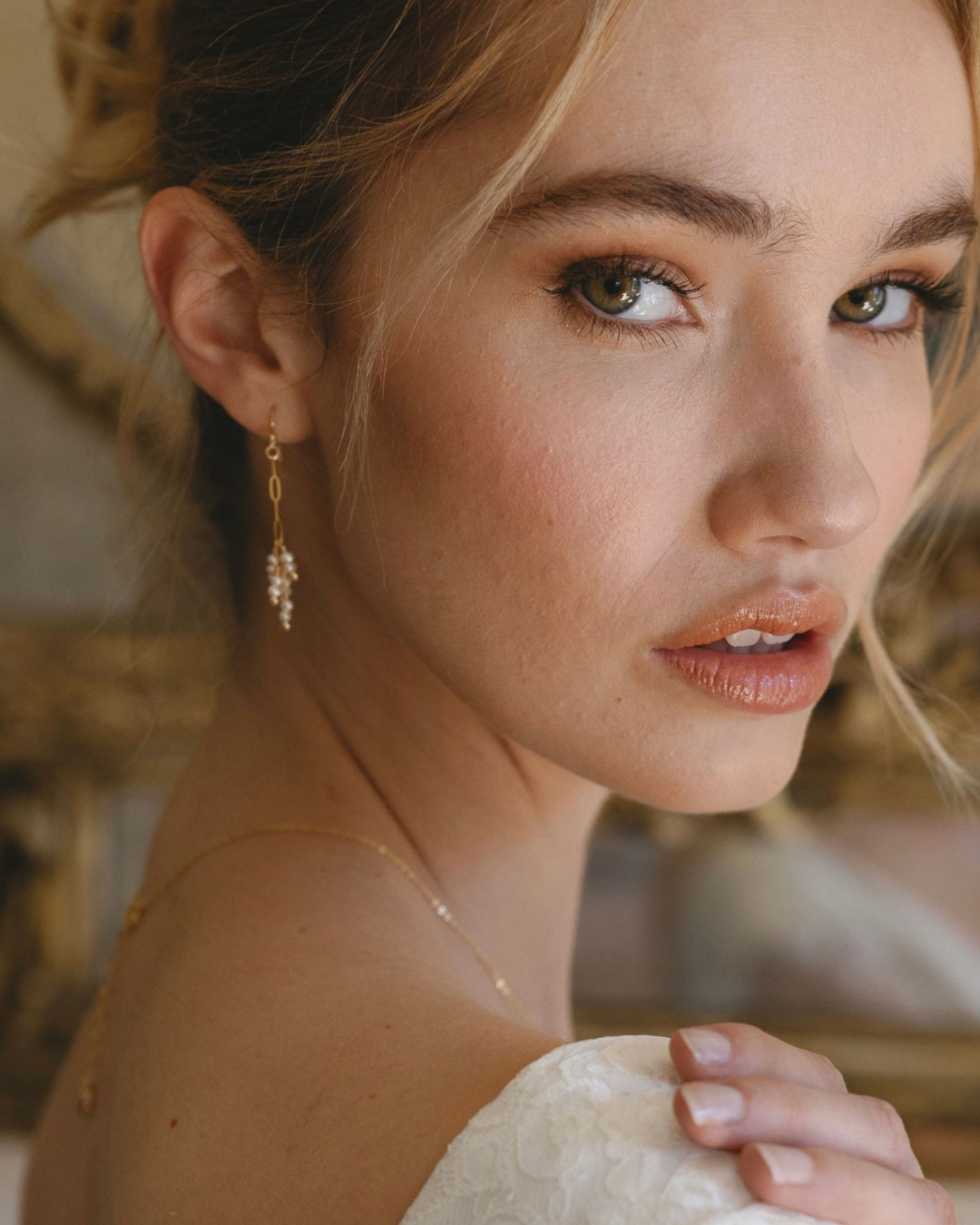 Close-up of a bride wearing a delicate gold and pearl earring and necklace.