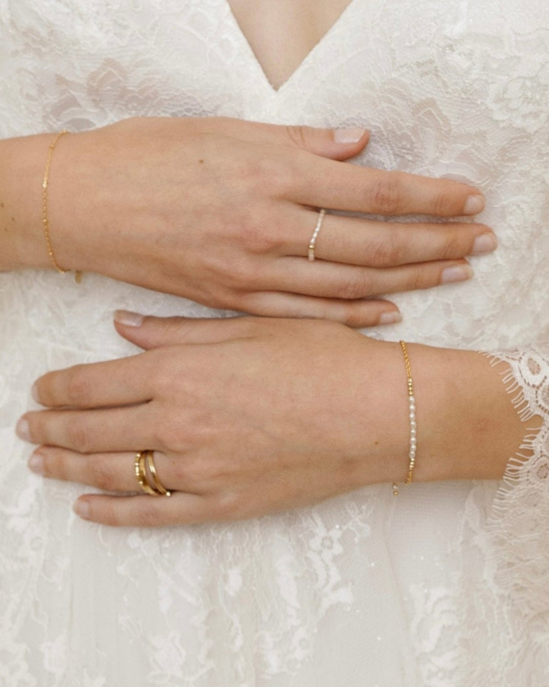 Close up of hands of bride wearing gold an pearl rings and bracelets on a white lace background