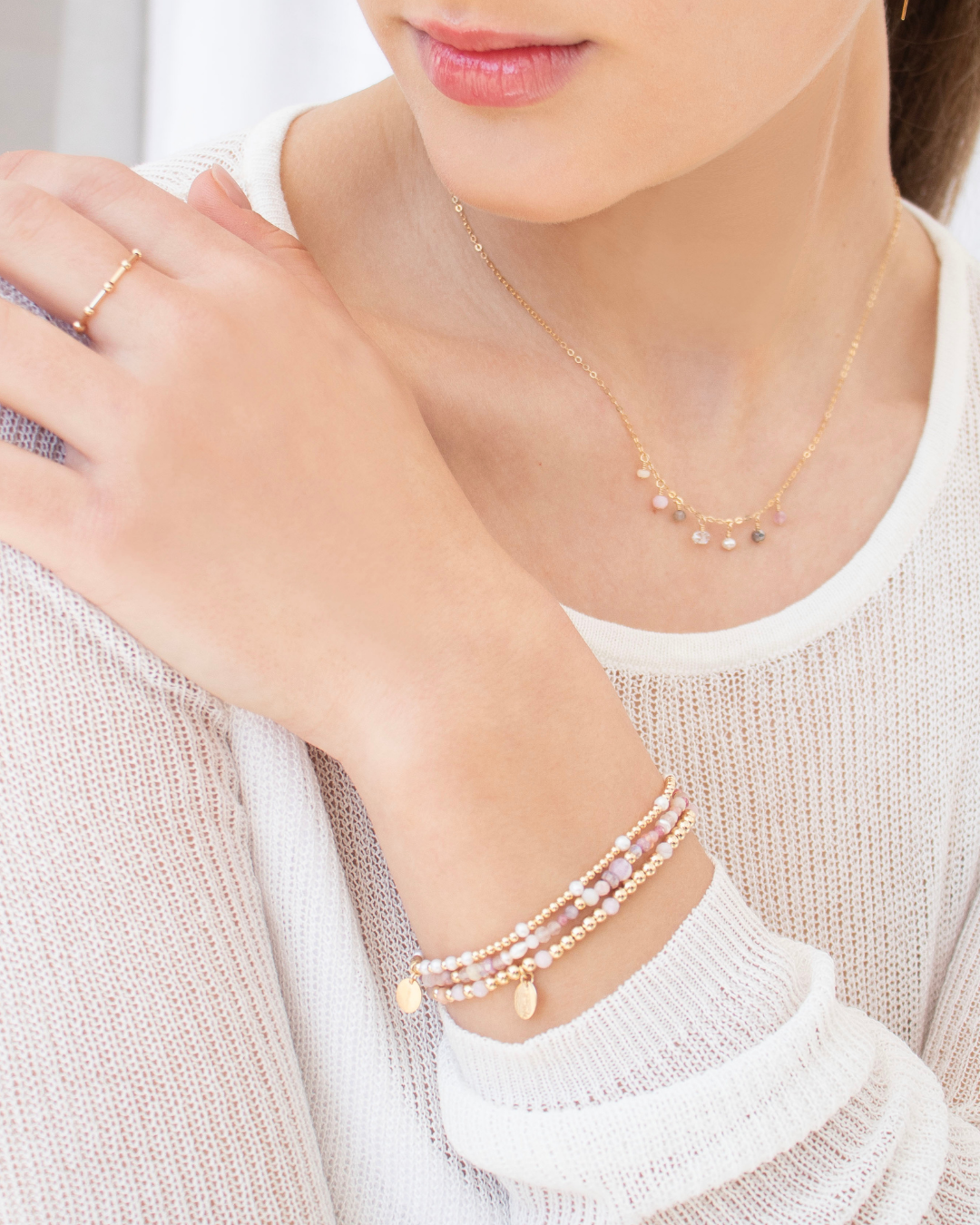 Close-up of a person wearing pearl bracelets, a necklace and ring with a neutral background