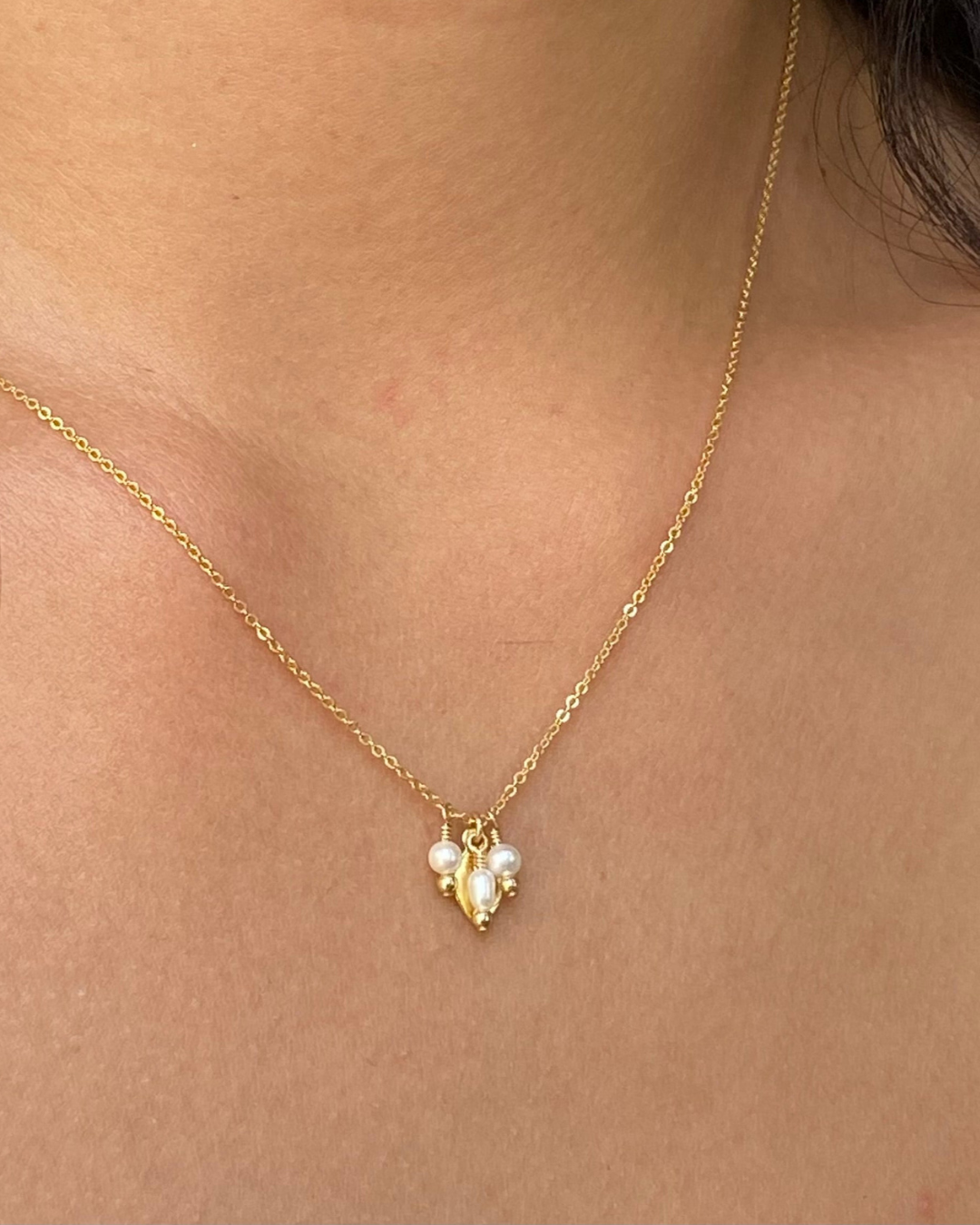 Gold necklace with a pendant featuring pearls on a person's neck.