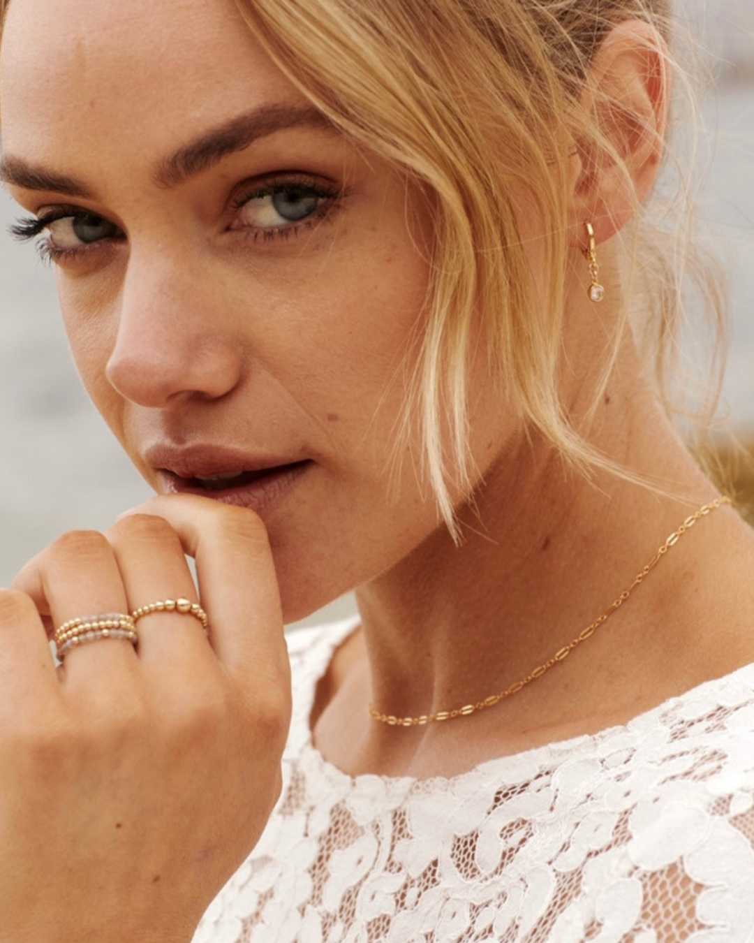 Close-up of a woman wearing gold jewelry including cubic zirconia hoop earrings, gold necklace and rings.