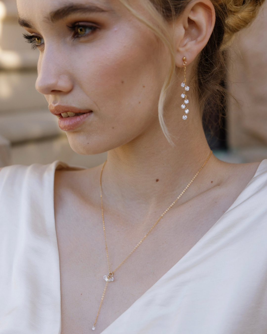 Close-up of a bride in wedding dress wearing gold and Cubic Zirconia Drop earrings and necklace with a blurred background