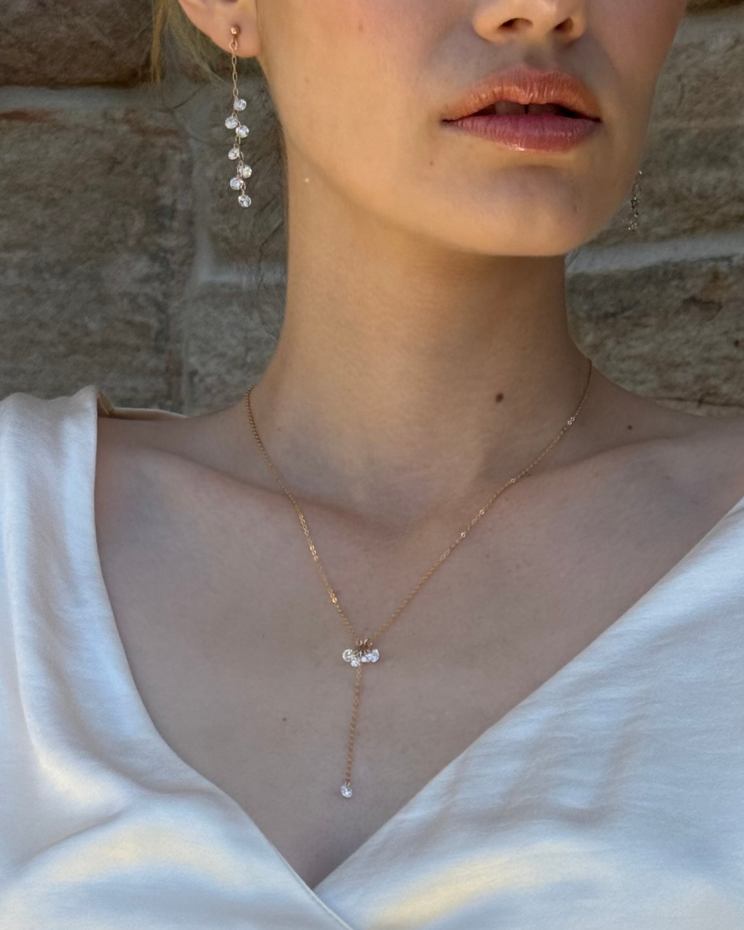 Close-up of a bride wearing a delicate lariat necklace and earrings with gold and Cubic Zirconia Drops.