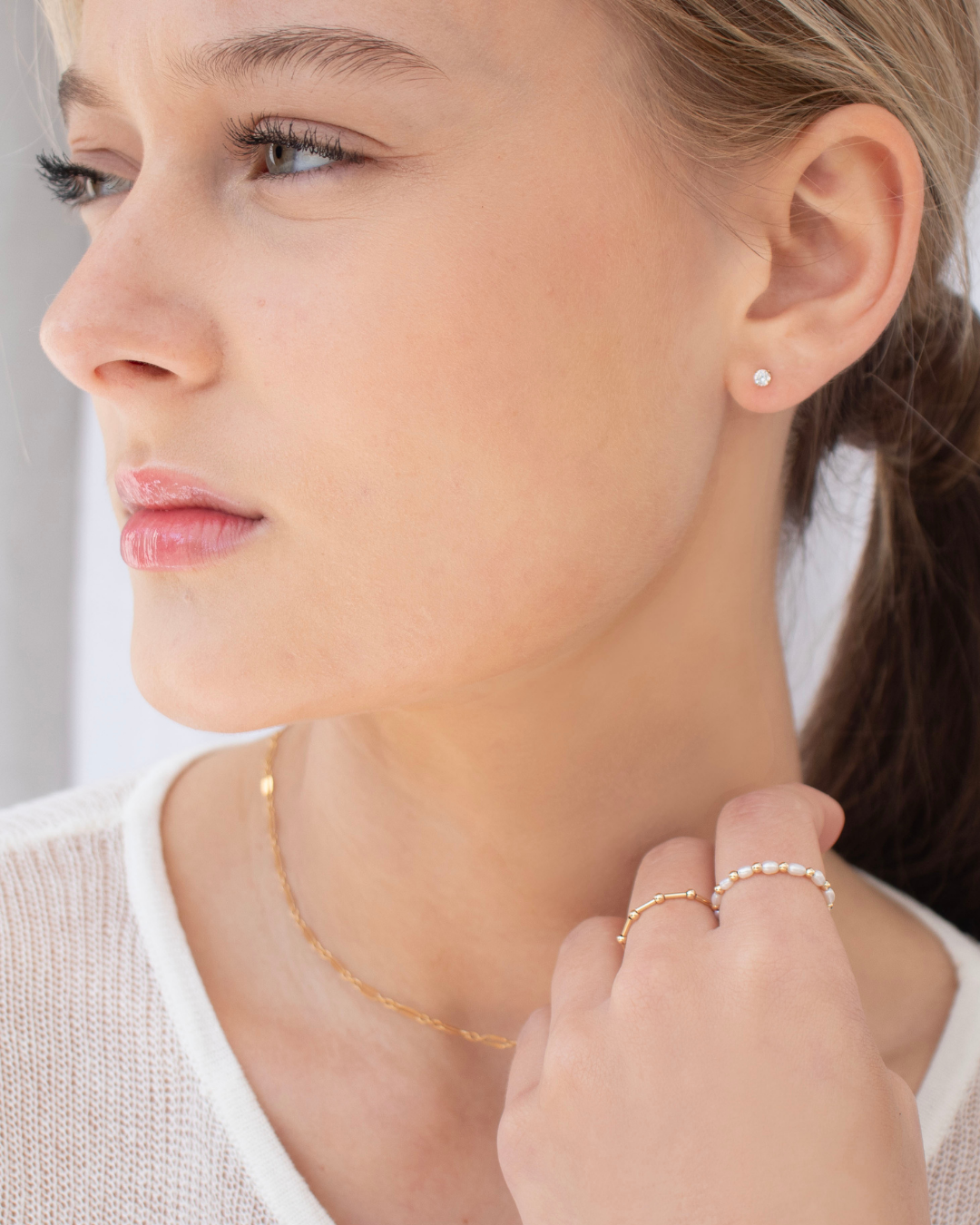 Close-up of a woman wearing gold jewellery including cubic zirconia stud earrings, gold necklace and rings.