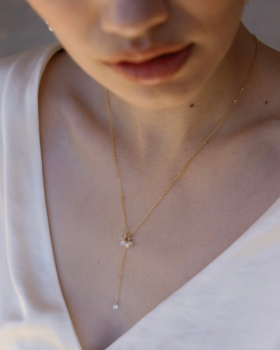 Close-up of a bride's neck with a delicate gold and cubic zirconia lariat necklace.