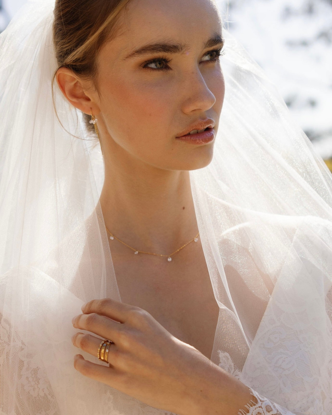 Bride wearing a white veil with a gold and cubic zirconia gemstone necklace and earrings and gold rings.