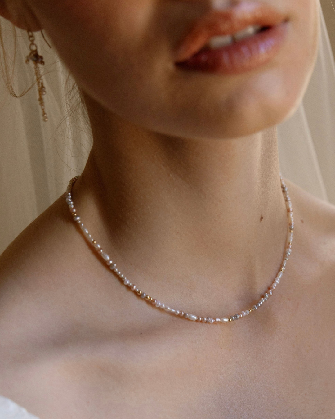 Close-up of a bride wearing a delicate pearl necklace with a neutral background