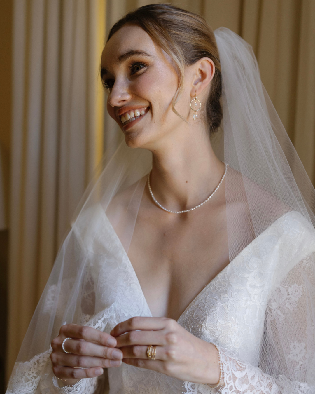 Bride wearing a veil and jewelry, smiling indoors.