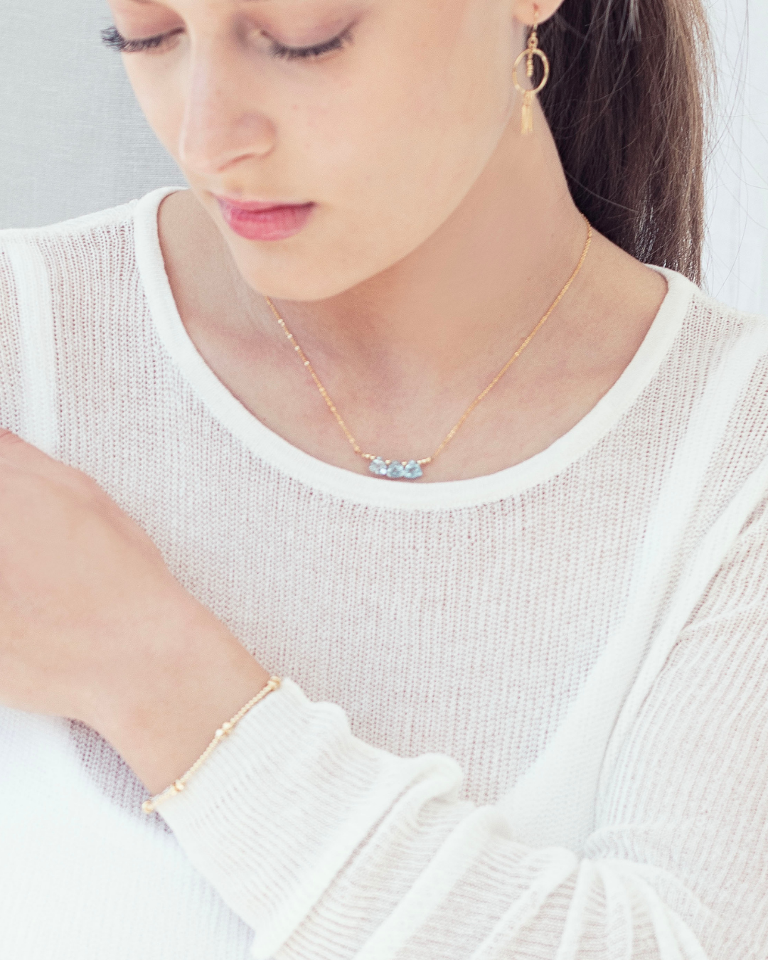 Close up of a woman wearing a delicate gold necklace with blue topaz briolette gemstones, gold bracelet and earrings.
