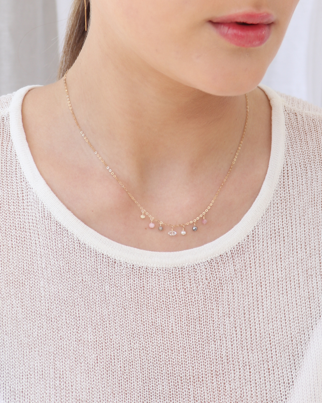 Close-up of a person wearing a delicate gold necklace with multiple gemstones in shades of pink and grey.