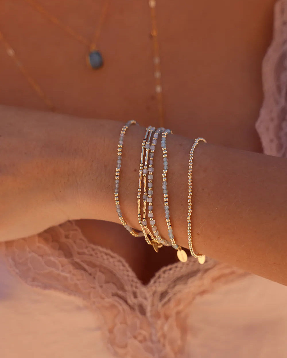 Model wearing bracelet with round gold beads and soft light blue Aquamarine cube gemstones, hand-threaded onto strong, durable elastic cord