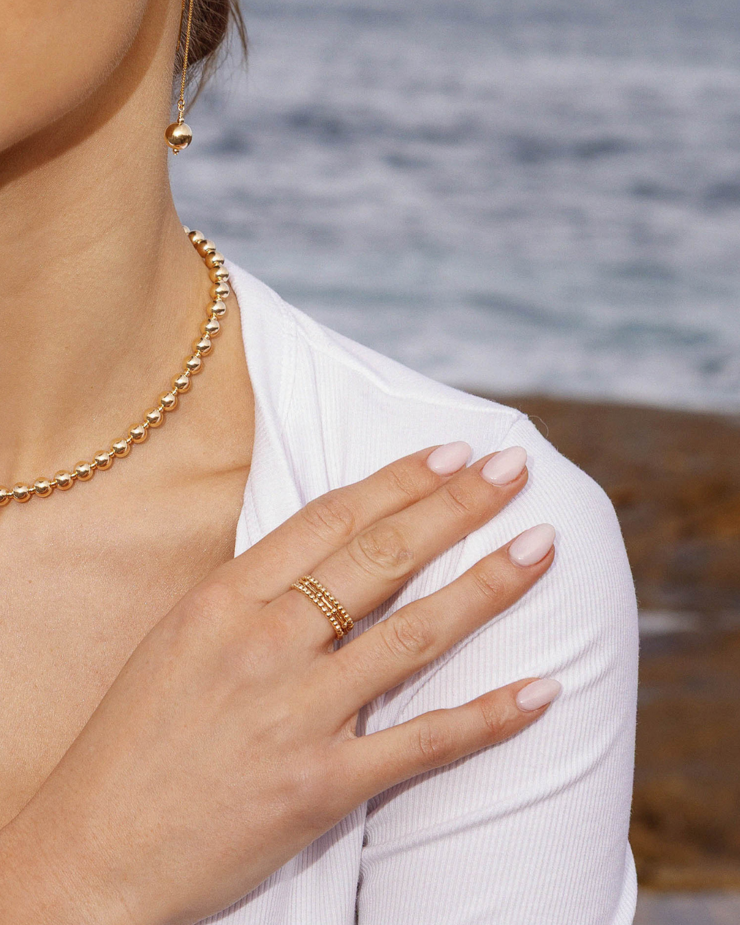 Close-up of a person wearing gold jewelry with a blurred beach background