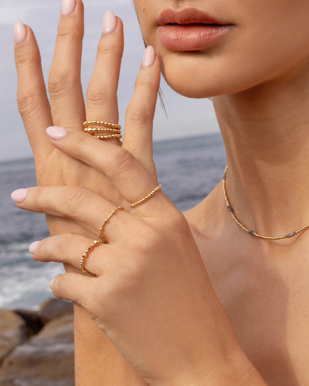 Close-up of a hand wearing gold rings with a blurred ocean background