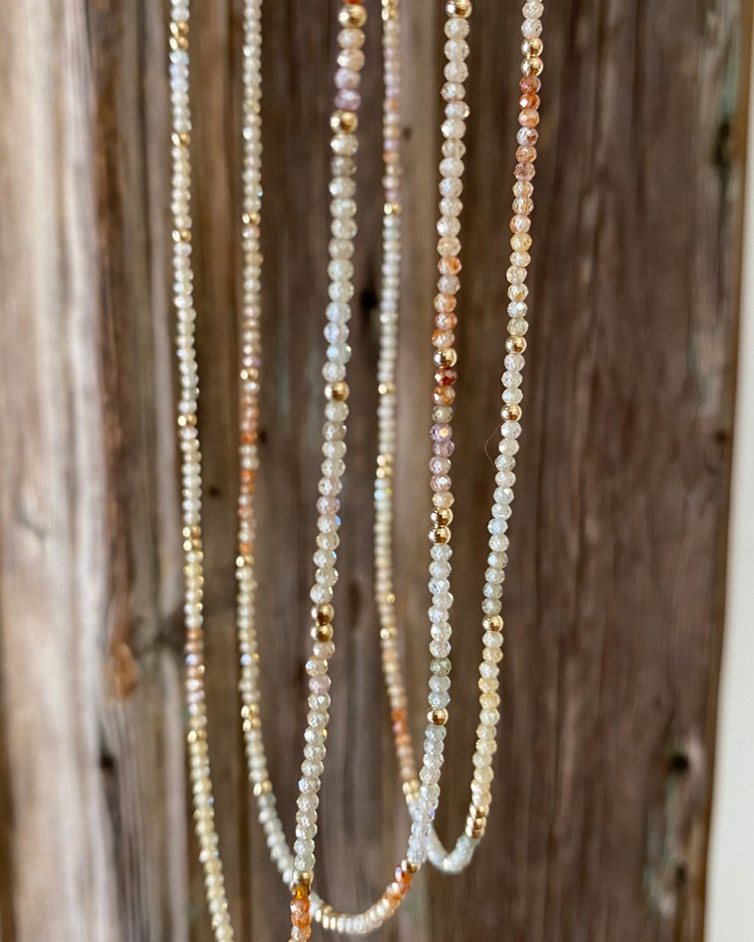 Three zircon gemstone beaded necklaces of different natural tones hanging against a wooden background