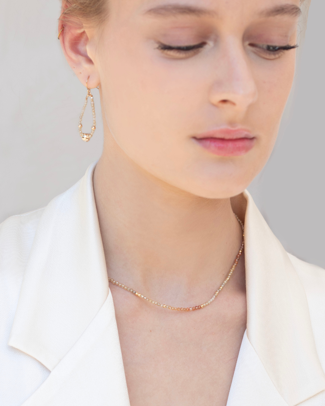 Close-up of a model wearing a delicate gold and zircon gemstone necklace and earrings against a neutral background