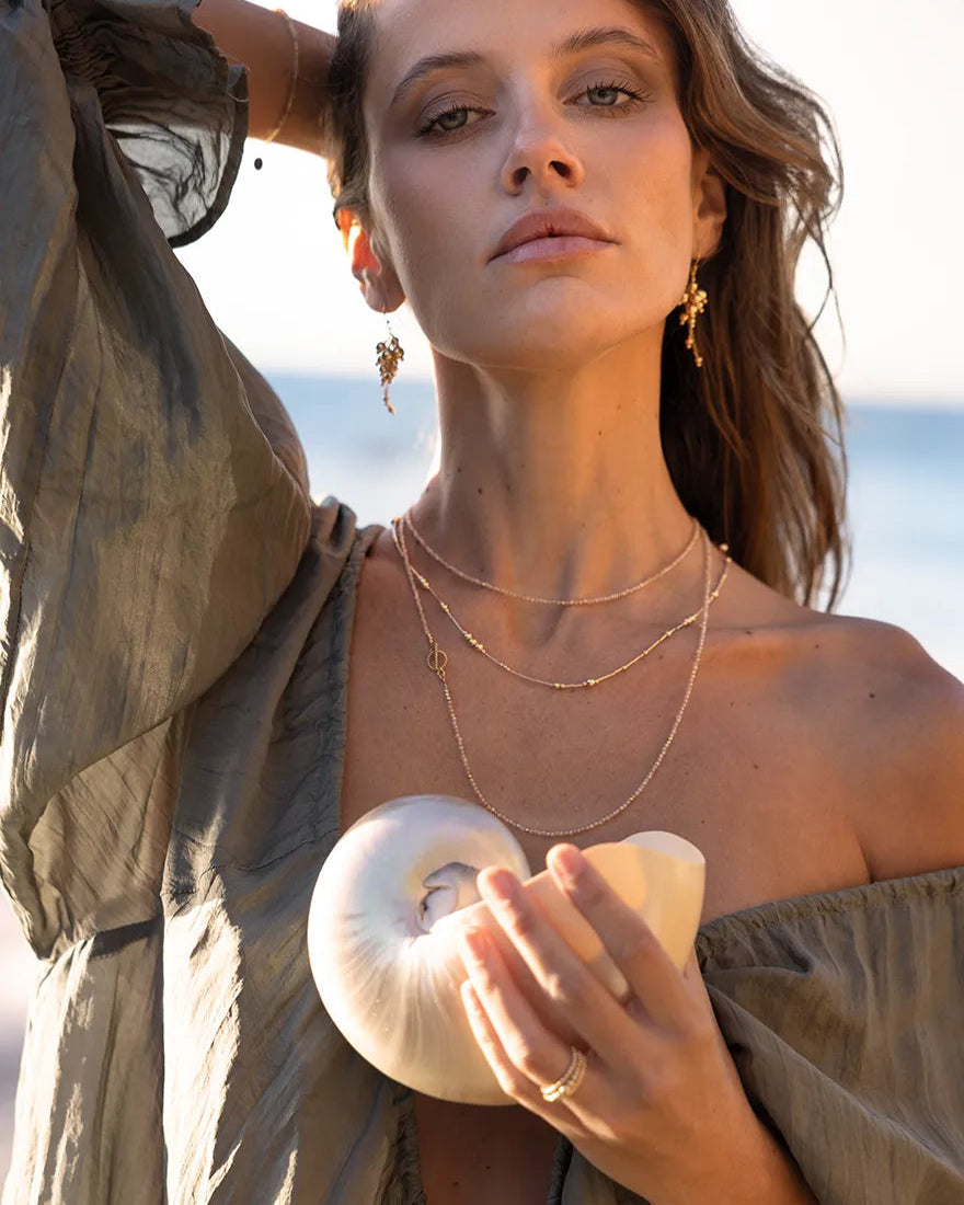 Model wearing necklace with fine gold tubes and smooth round gold beads in varying sizes