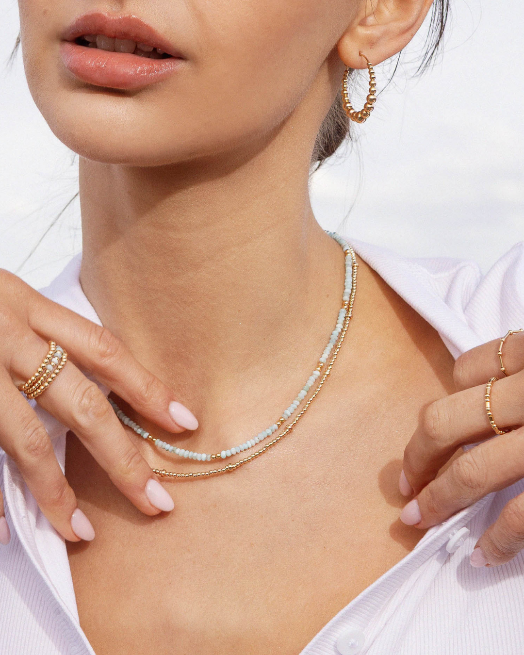 Close-up of a person wearing gold jewelry including a necklace, hoop earrings, and rings.