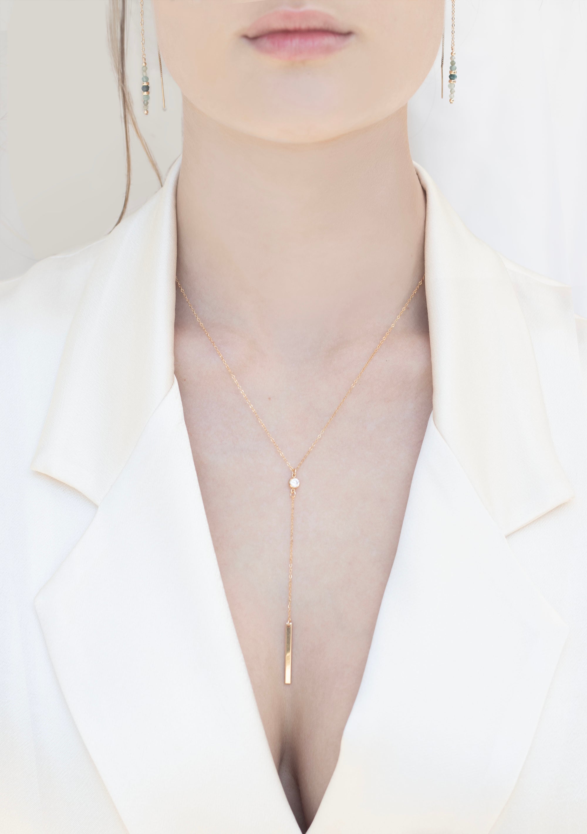 Gold cubic zirconia lariat necklace worn by a person in a white outfit