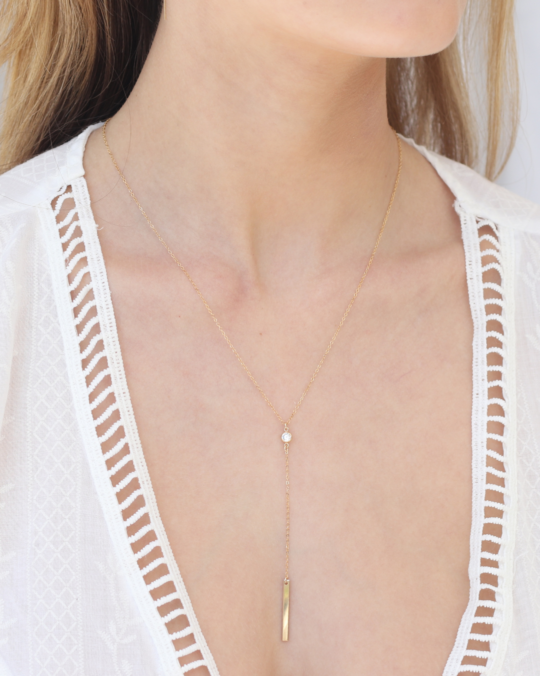 Gold lariat necklace featuring a cubic zircon gemstone worn by a woman in a white outfit.