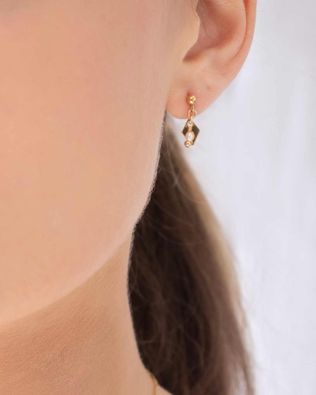 Gold earring with a fresh water pearl worn by a bride with a neutral background