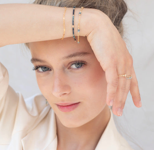 Woman wearing multiple bracelets on her wrist with a neutral background