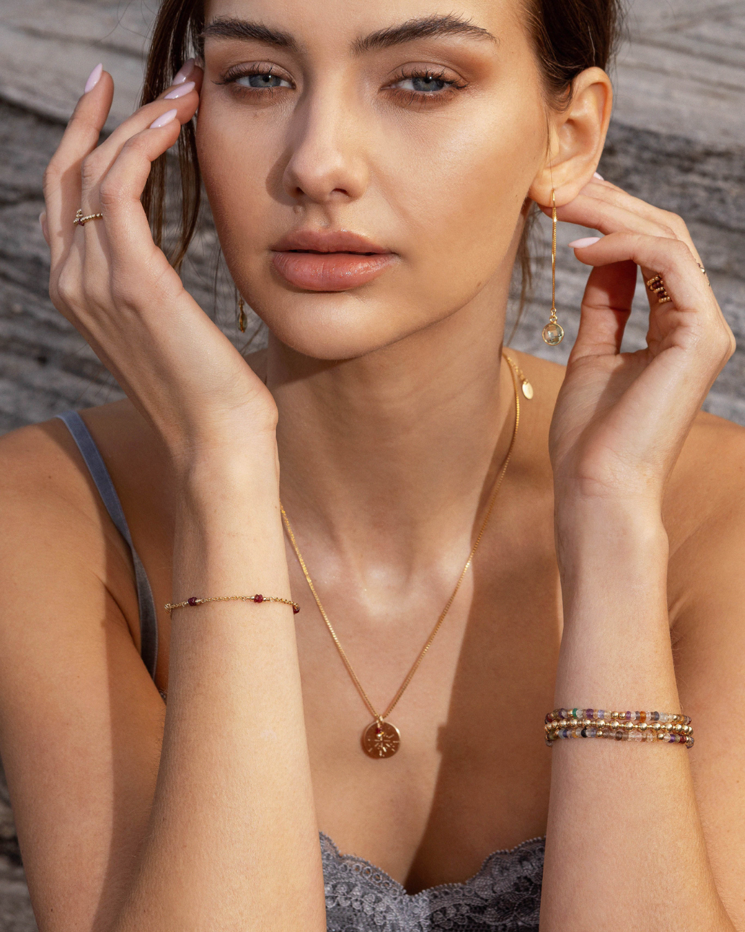 Woman wearing gold jewelry including a necklace, earrings, and ruby bracelet against a neutral background