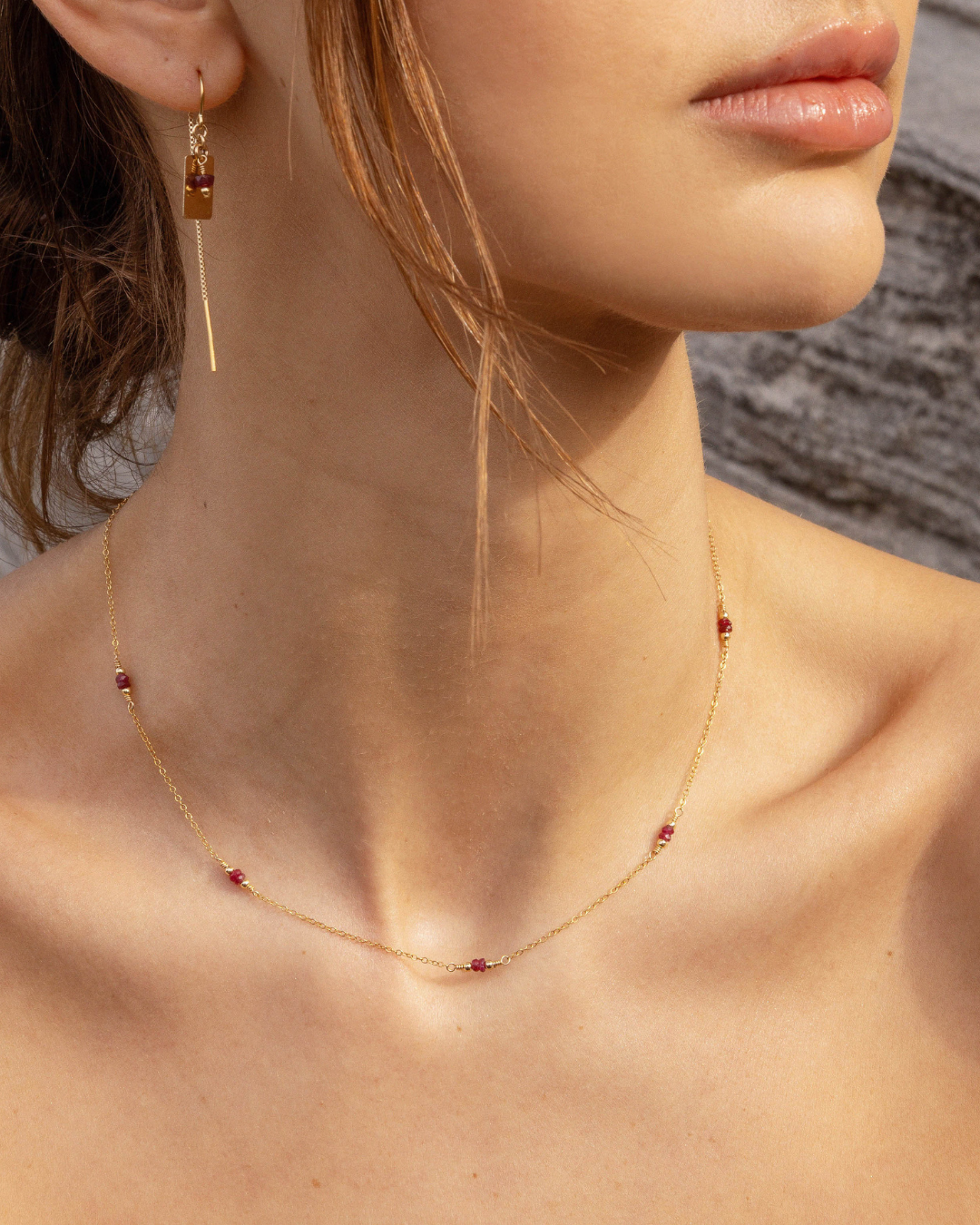 Close-up of a woman wearing gold and ruby gemstone necklace and thread earrings.