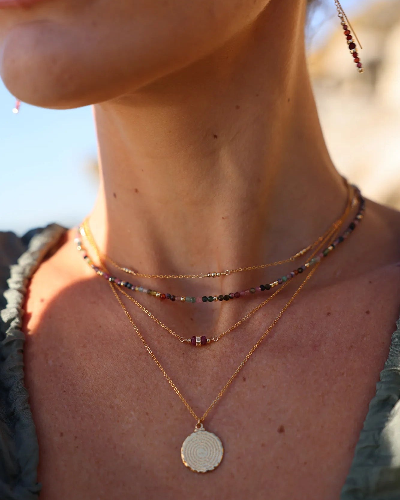 Model wearing multi coloured tourmaline gemstone and gold beaded necklace layered with other necklaces