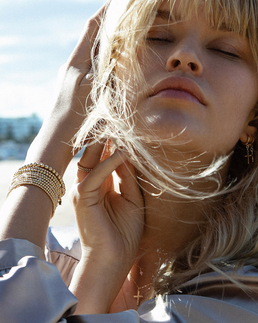 Woman with blonde hair and gold jewellery against a blurred natural background