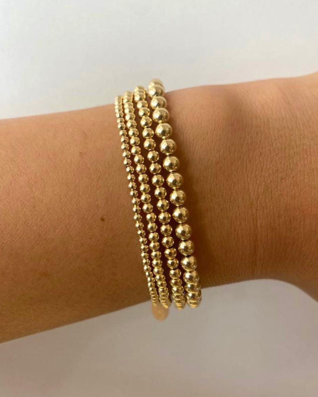 Gold beaded bracelets on a wrist against a white background