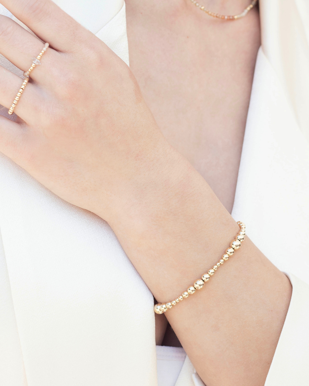Gold beaded bracelet on a wrist with a plain background