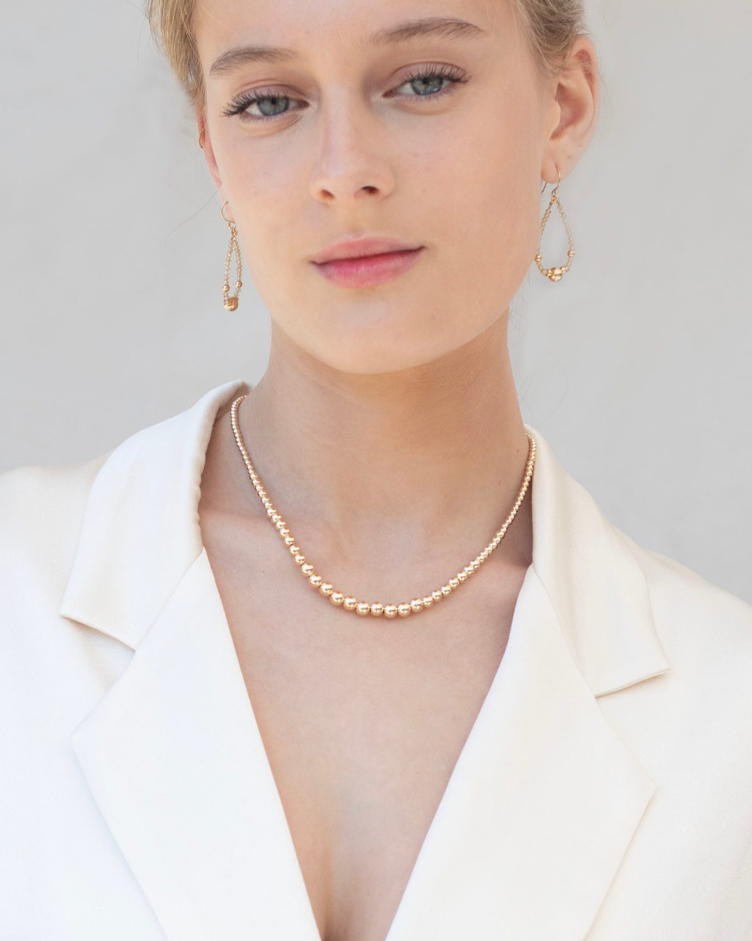 Woman wearing a gold necklace and zircon gemstone earrings on a plain background