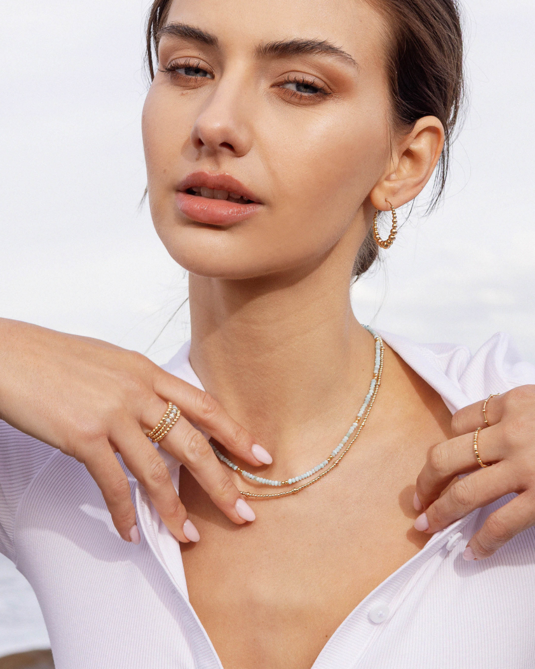 Woman wearing a gold necklaces, rings, and hoop earrings with a white background