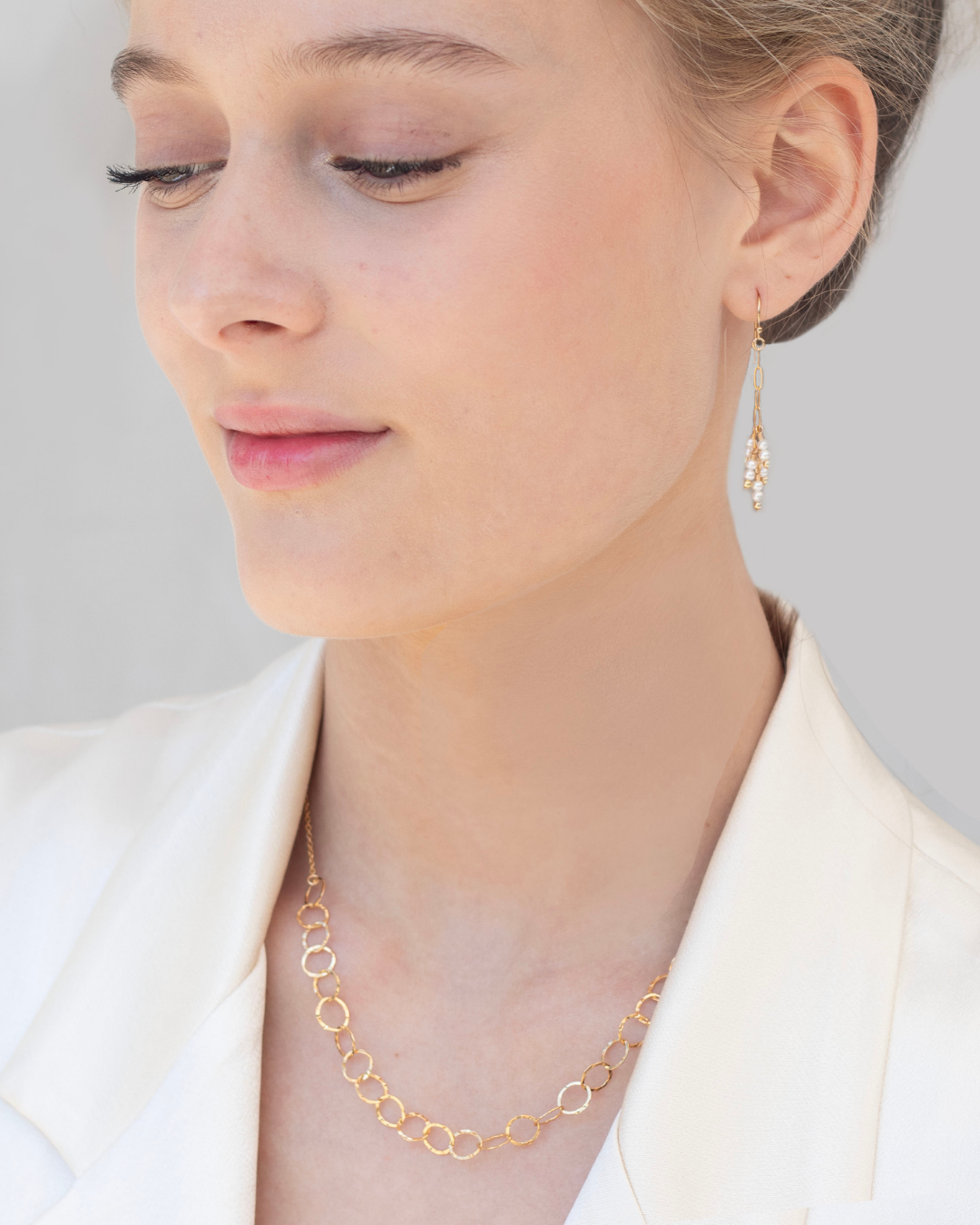 Close-up of a woman wearing gold and pearl earrings with a gold necklace against a neutral background